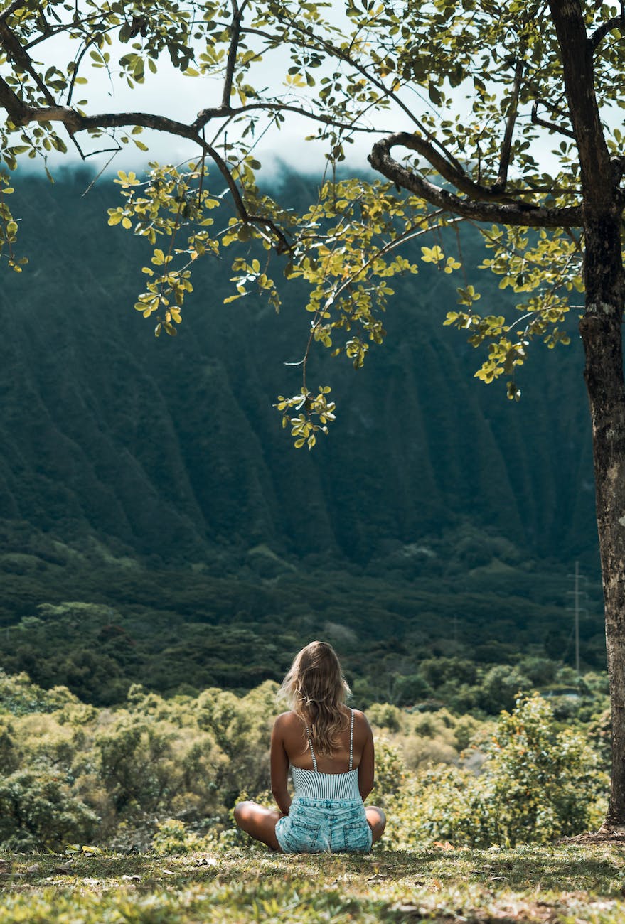 unrecognizable female meditating on grass in highlands on sunny day